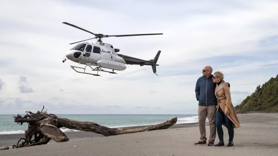 Couple watching helicopter land on a remote West Coast beach in New Zealand