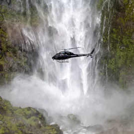 Helicopter flying close to the misty base of Sutherland Falls in Fiordland