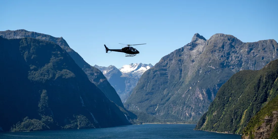 Helicopter flying above Milford Sound with dramatic mountain cliffs