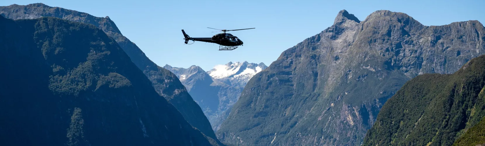 Helicopter flying above Milford Sound with dramatic mountain cliffs