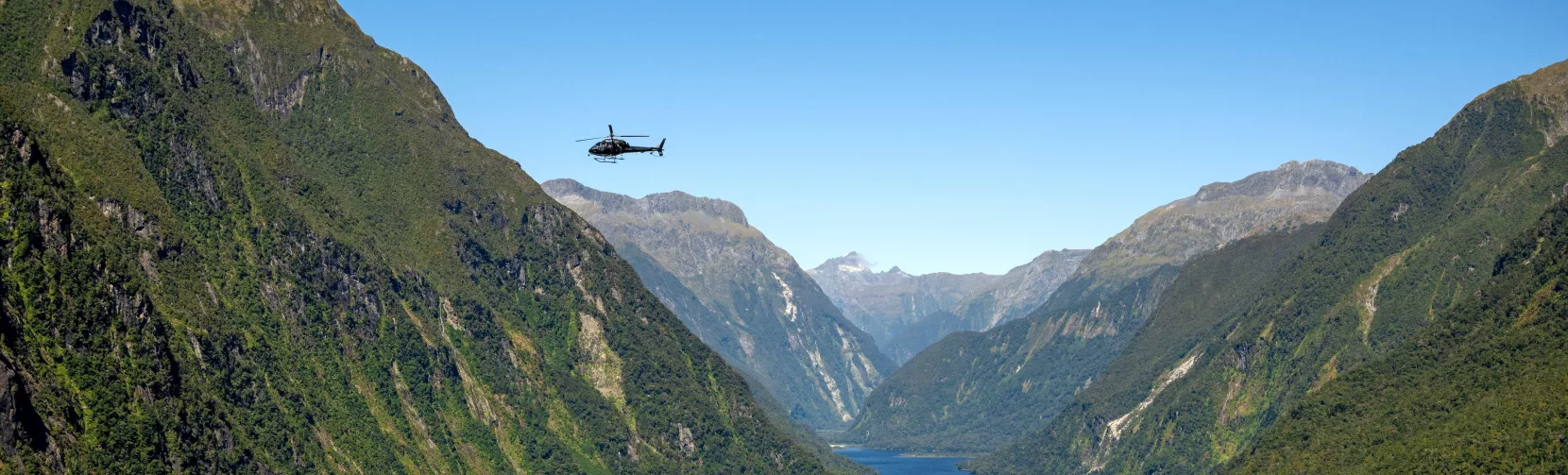 Helicopter flying above the lush cliffs and winding waters of Milford Sound