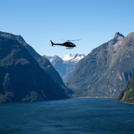 Helicopter flying above Milford Sound with dramatic mountain cliffs