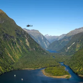 Helicopter flying above the lush cliffs and winding waters of Milford Sound