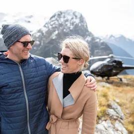 Couple smiling in front of a helicopter landing in the Southern Alps