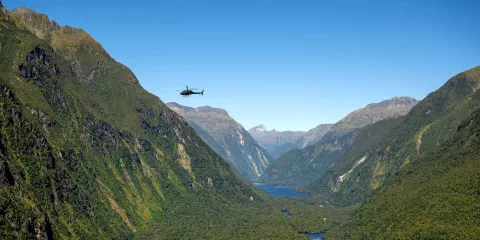 Helicopter flying above the lush cliffs and winding waters of Milford Sound