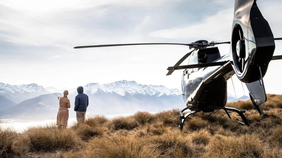 Couple standing beside a helicopter with snow-capped peaks of the Southern Alps in the background