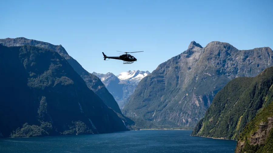 Helicopter flying above Milford Sound with dramatic mountain cliffs