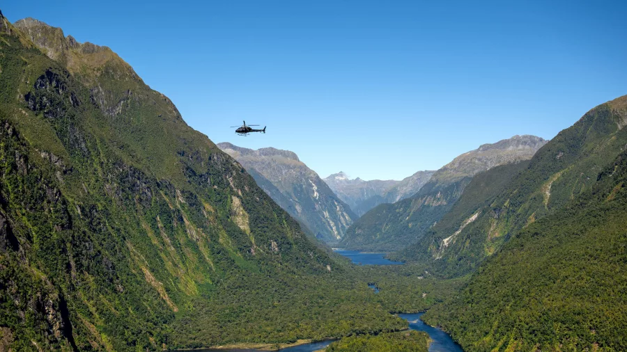 Helicopter flying above the lush cliffs and winding waters of Milford Sound