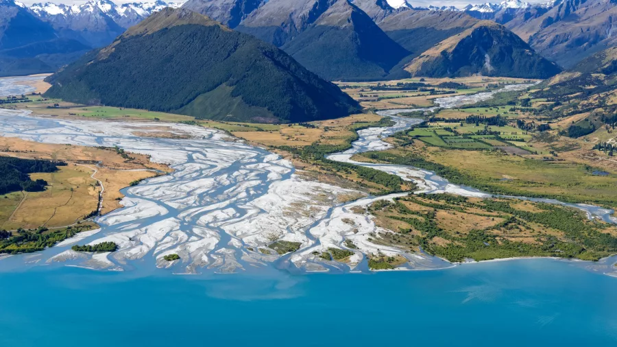 Helicopter flying over Glenorchy river deltas with mountain ranges in the distance