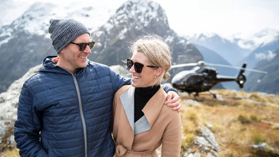 Couple smiling in front of a helicopter landing in the Southern Alps