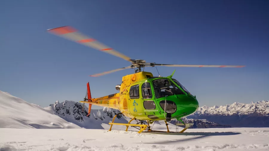 Heli Glenorchy helicopter parked on alpine snow with clear blue skies