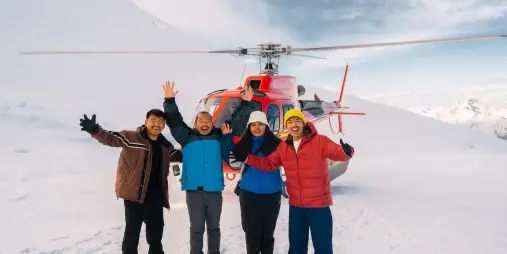 Group of guests standing in the snow beside a red helicopter near Glenorchy.
