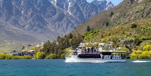 Million Dollar Cruise boat carrying passengers across Lake Wakatipu, with the towering Remarkables mountain range in the background.