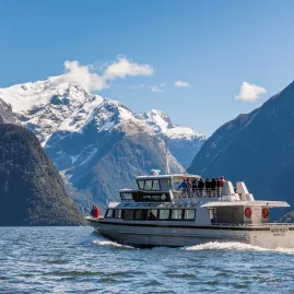 Mitre Peak Cruises boat sailing through Milford Sound with snowy mountain backdrop