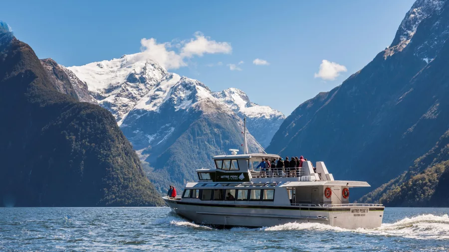 Mitre Peak Cruises boat sailing through Milford Sound with snowy mountain backdrop