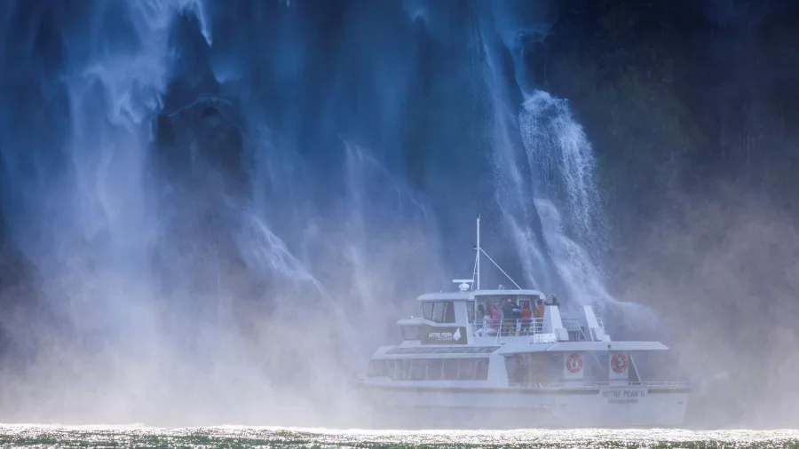 Cruise boat in the mist of a thundering Milford Sound waterfall