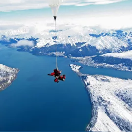 Tandem skydivers descending over a snow-covered Queenstown and Lake Wakatipu