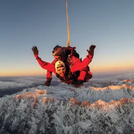 Tandem skydivers over snow-covered mountains at sunset near Queenstown