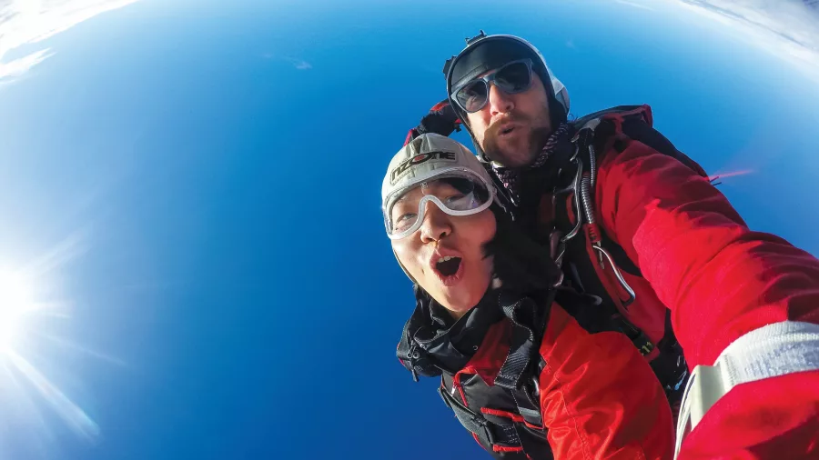 Tandem skydiving selfie with blue sky and wide-angle view above Queenstown