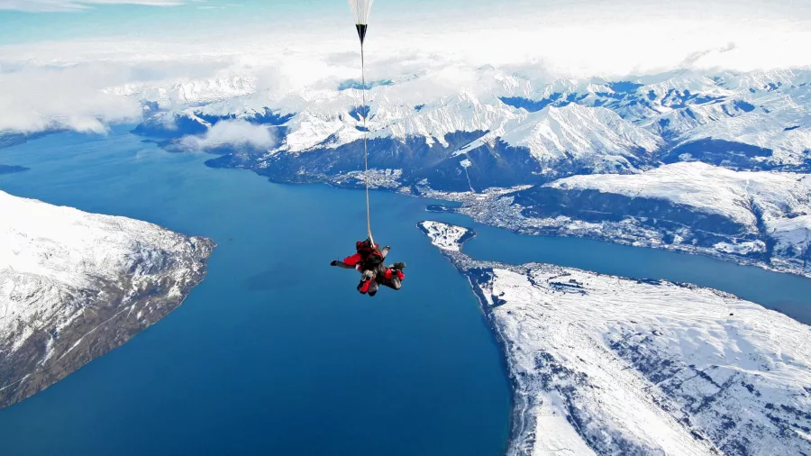 Tandem skydivers descending over a snow-covered Queenstown and Lake Wakatipu