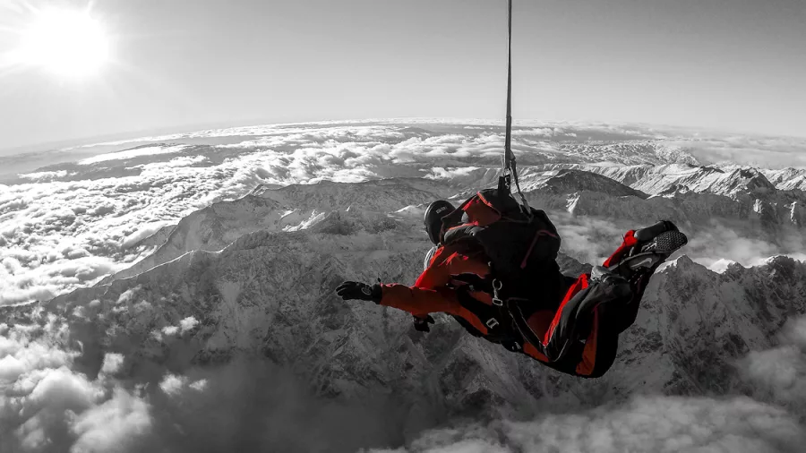 Black and white skydiving photo with red jumpsuit and cloudscape