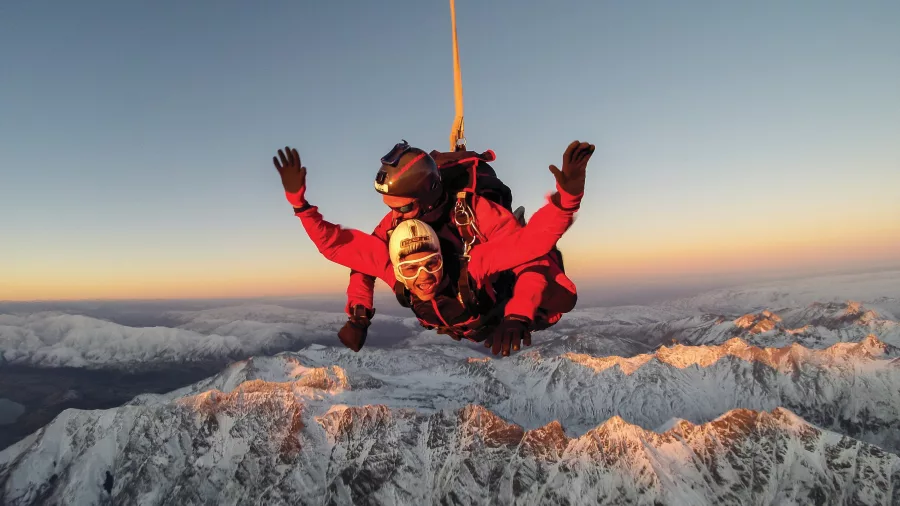 Tandem skydivers over snow-covered mountains at sunset near Queenstown