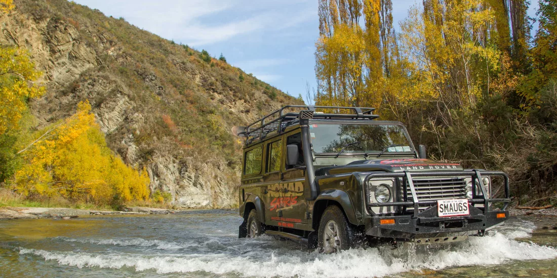 Nomad Safaris 4WD vehicle crossing shallow river in autumn colours