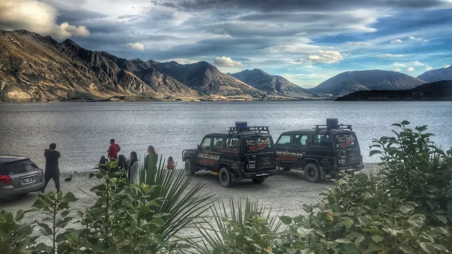Nomad Safaris Land Rovers parked beside Lake Wakatipu with scenic mountains in the background