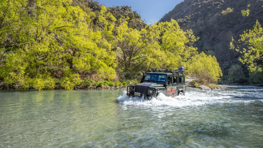 4WD Land Rover splashing through clear water with bright green trees in Queenstown