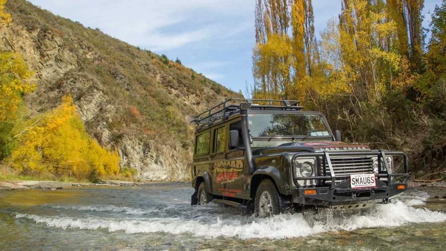 Nomad Safaris 4WD vehicle crossing shallow river in autumn colours