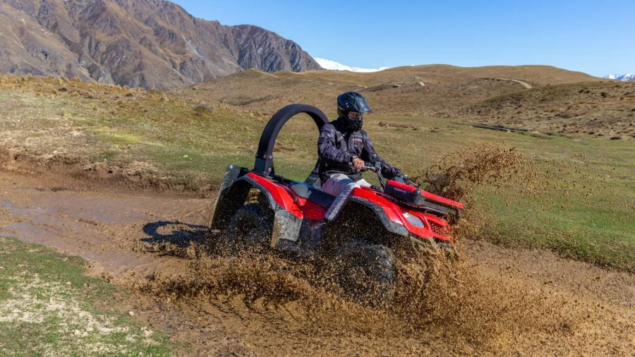 Rider splashing through muddy water on a quad bike in Queenstown hills