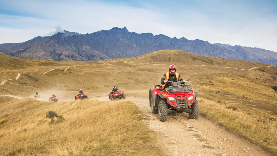 Group riding quad bikes along dirt trail with The Remarkables in the background