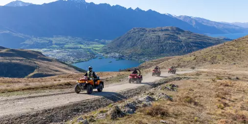 Group of quad bikers riding uphill overlooking Lake Wakatipu and Queenstown