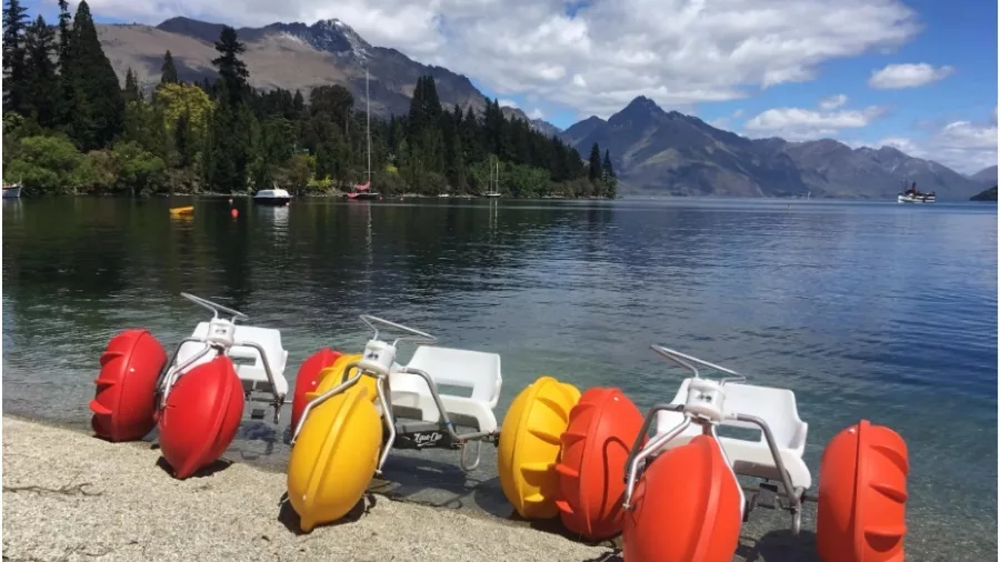 Colourful aqua bikes lined up on the beach in Queenstown with scenic mountain views