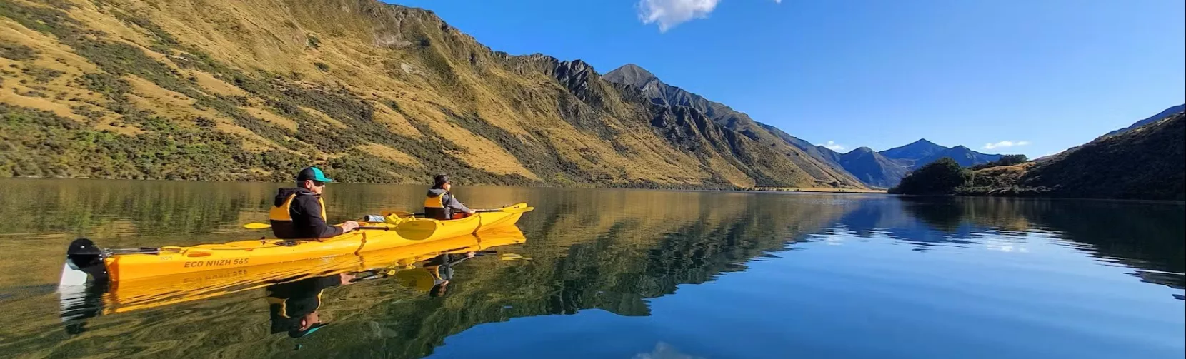 Two people in a tandem kayak gliding across Moke Lake with clear reflections
