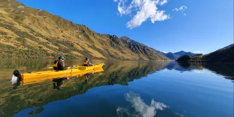 Two people in a tandem kayak gliding across Moke Lake with clear reflections