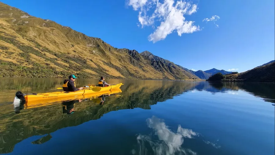 Two people in a tandem kayak gliding across Moke Lake with clear reflections