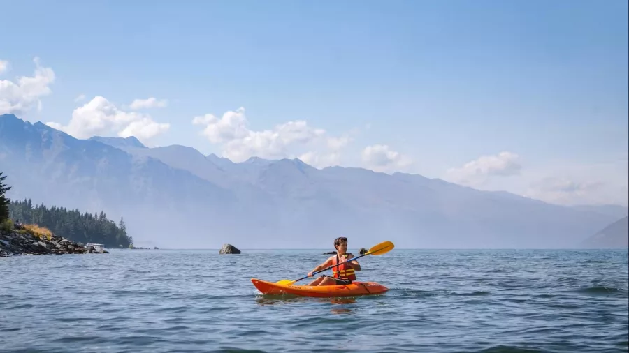 Young person kayaking on open water with mountains and trees in the distance