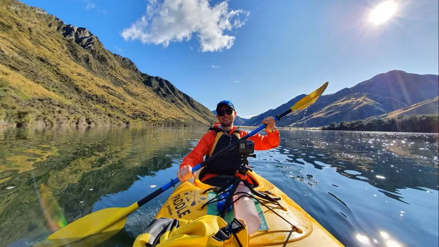 Man kayaking on Moke Lake during a guided tour with sun and mountain reflections