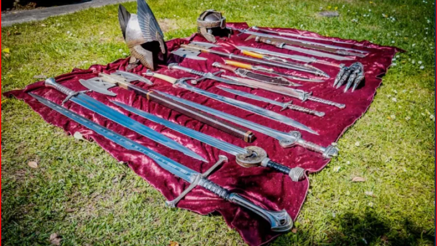 Collection of Lord of the Rings swords, helmets and props laid out on red velvet