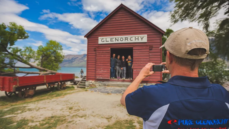 Tour group posing at the historic Glenorchy red shed while Pure Glenorchy guide takes a photo
