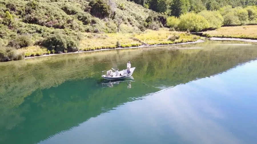 Drift boat with fly fisherman on a calm lake near Queenstown, surrounded by bush
