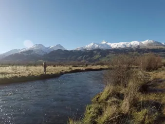 Angler fly fishing in a scenic river with snow-capped mountains near Queenstown