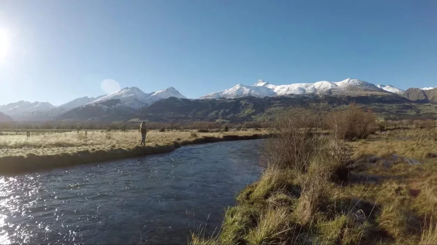 Angler fly fishing in a scenic river with snow-capped mountains near Queenstown