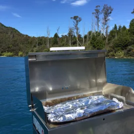 Foil-wrapped fish cooking on a barbecue aboard a boat on Lake Wakatipu