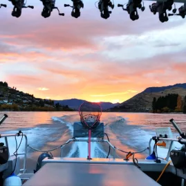 Fishing boat speeding across Lake Wakatipu at sunset with gear and mountains in view