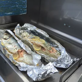 Two whole trout wrapped in foil with lemon, cooking on a barbecue on a fishing boat