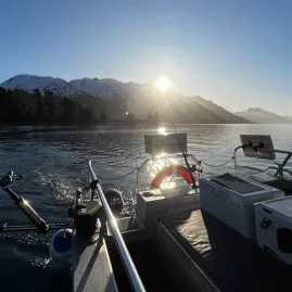 Fishing rods on a boat at sunrise with snowy mountains around Lake Wakatipu