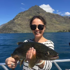 Smiling woman holding a brown trout with Queenstown’s mountains behind