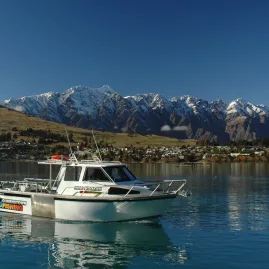 Fishing boat with Queenstown Fishing branding on Lake Wakatipu with snowy mountains in the background